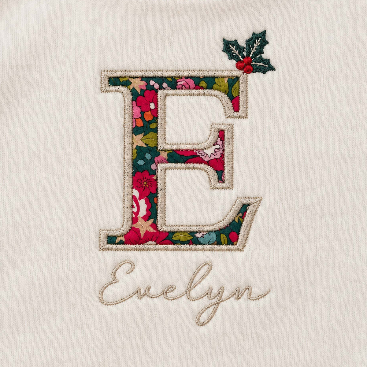 Close-up of Liberty fabric initial E with embroidered holly sprig and baby's name in script lettering