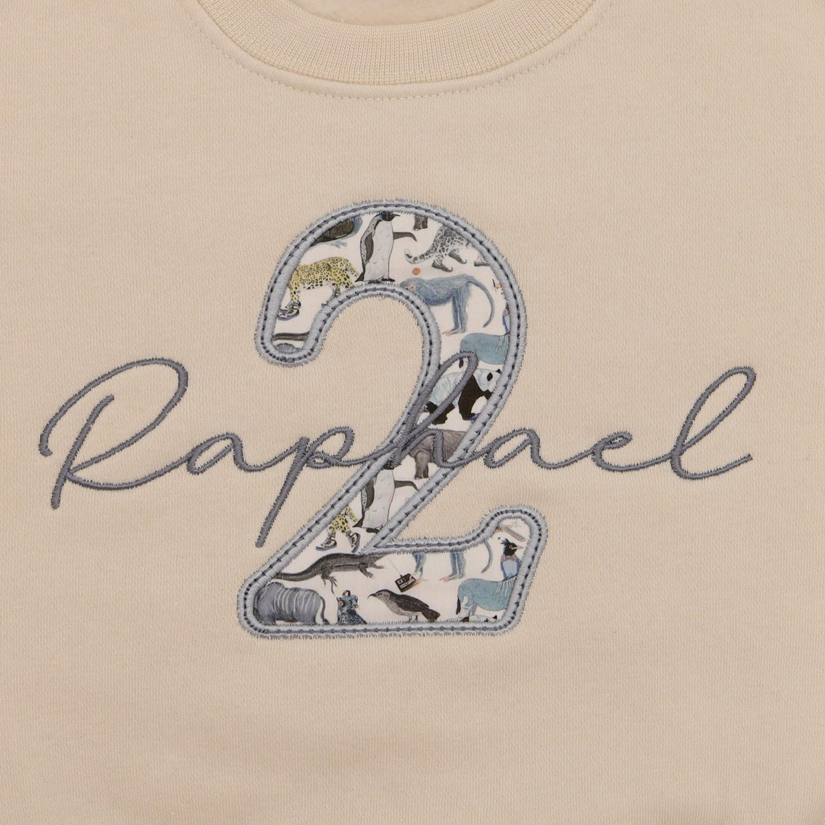 Close-up of script name embroidered across a Liberty fabric number 2 on an oat jumper