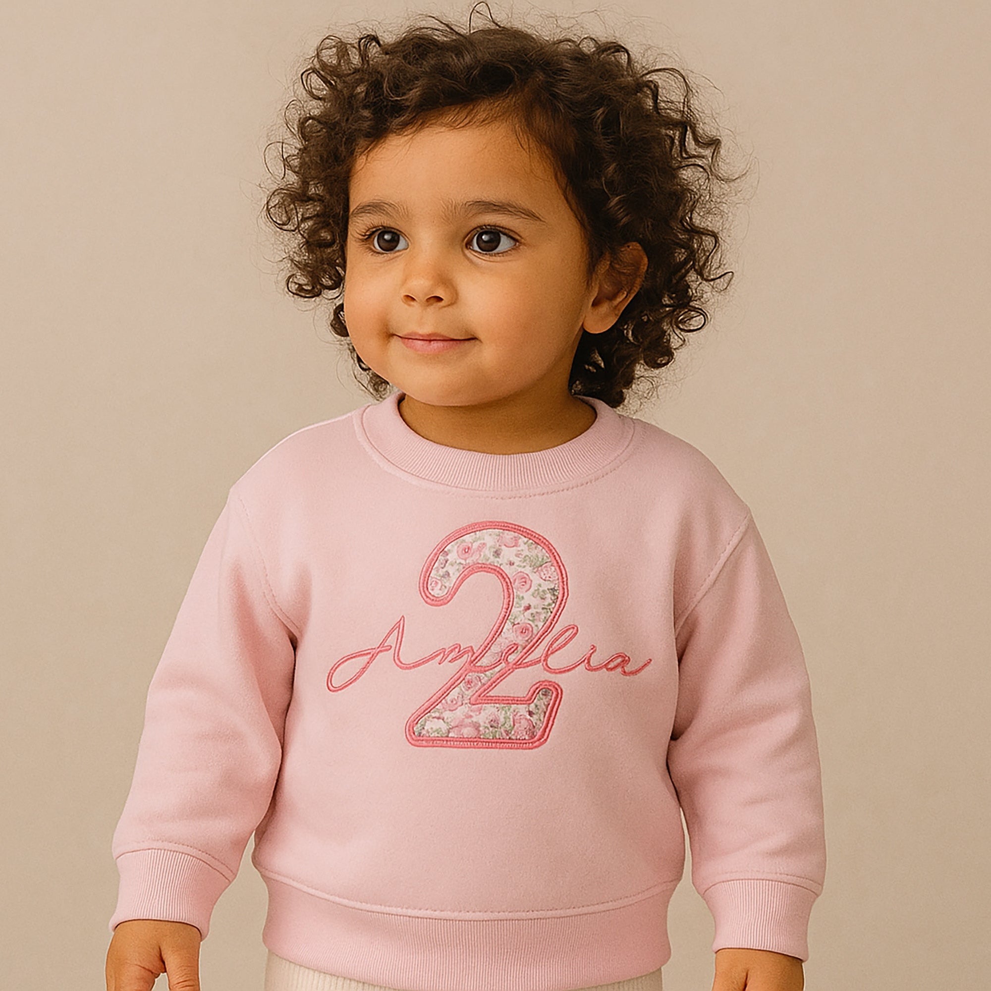 Child wearing a pink sweatshirt with 'Amelia 2' on a beige background