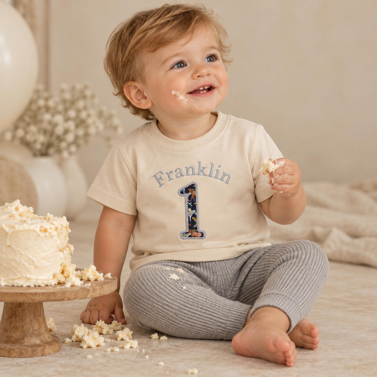 Boy wearing natural first birthday t-shirt with name above a Liberty fabric number 1