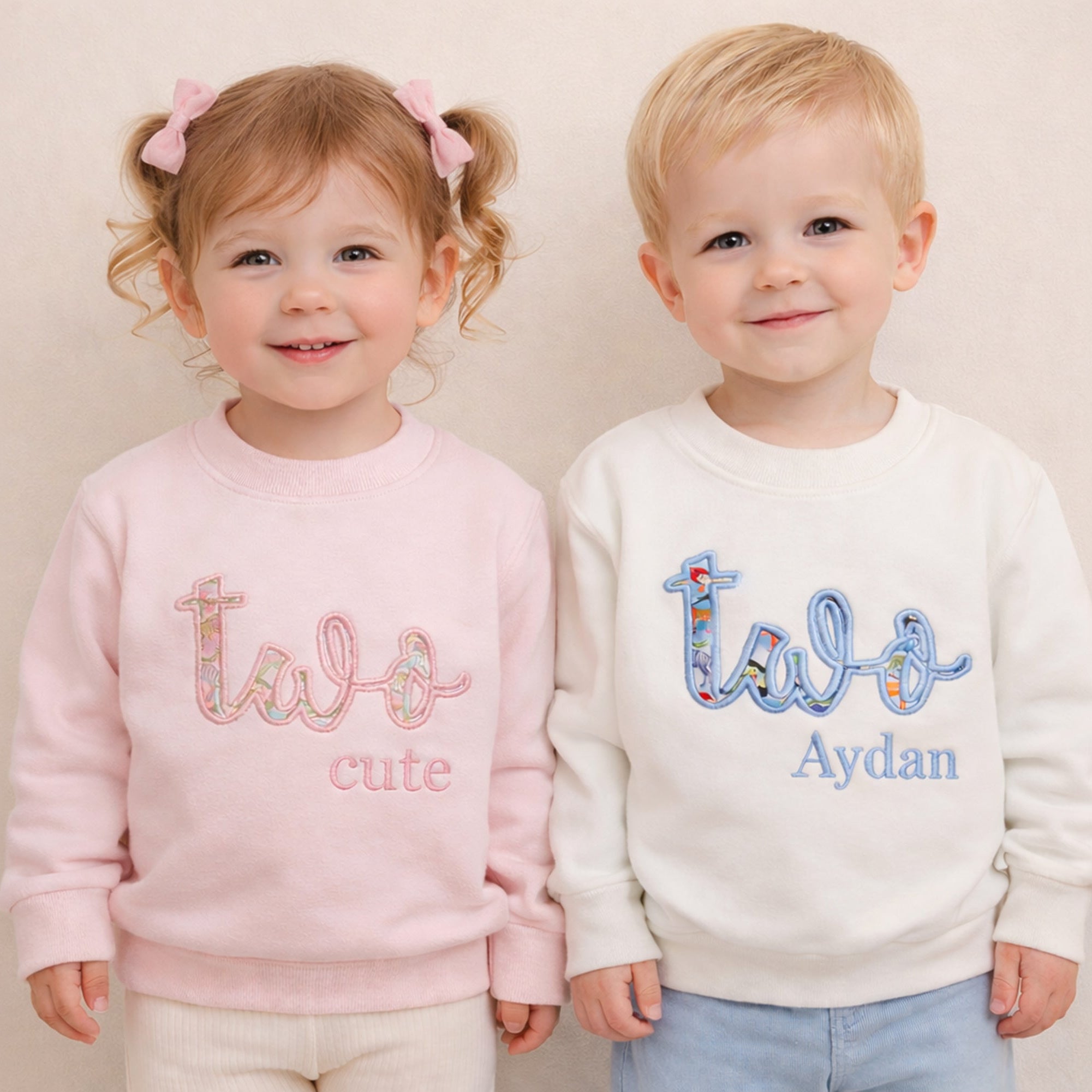 Two children wearing two cute personalised jumpers won a plain background